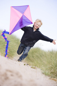 小男孩带着风筝在沙滩上奔跑