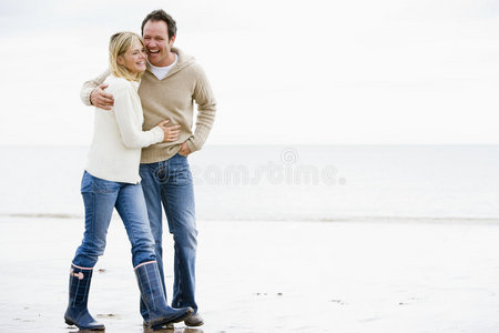 一对手挽手走在沙滩上微笑的夫妇