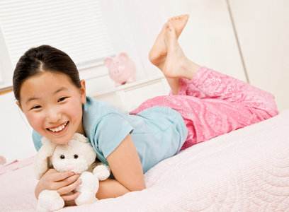 快乐的小女孩抱着毛绒玩具躺在床上