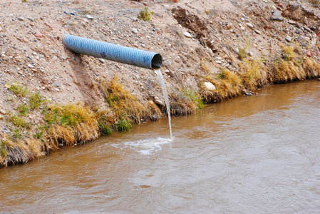 从管子流出的水炼油厂附近河在黄昏时分,商业和工业水管出水炼油厂