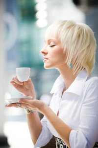 年轻的金发女人端着杯子，品尝着咖啡