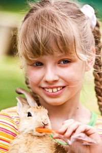 快乐的女孩用胡萝卜喂兔子。