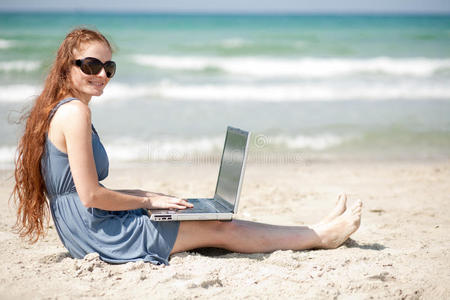 坐在海滩上用笔记本电脑工作的妇女