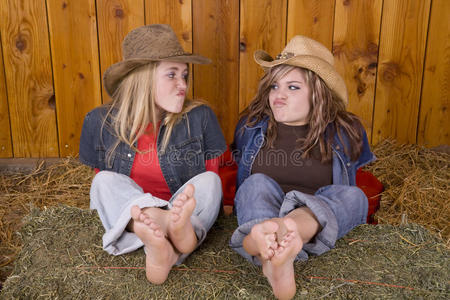 女孩们滑稽的脸脚踩在干草上照片