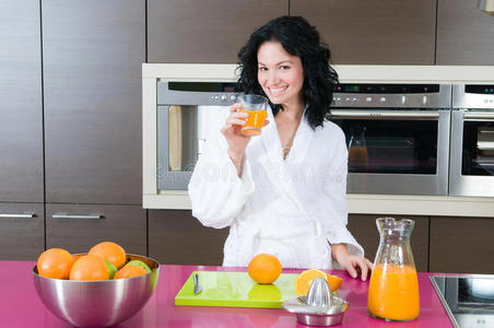 家庭厨房里拿着橙汁的快乐女人