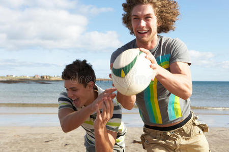 两个十几岁的男孩在海滩上玩橄榄球