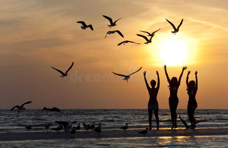 三个年轻女子日落时在海滩上跳舞
