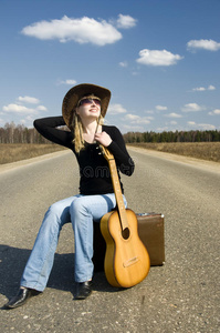 乡村女孩带着吉他独自坐在路上