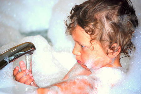 在泡泡浴里玩水龙头的小男孩