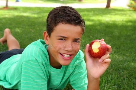 少年男孩在花园草地上吃红苹果