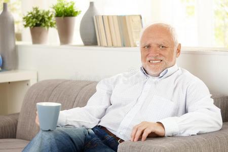 微笑的老人在沙发上喝咖啡