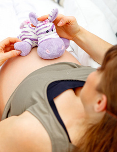 孕妇坐在沙发上，肚子上放着玩具
