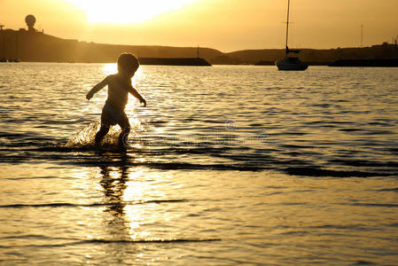 在金黄的夕阳下，一个蹒跚学步的孩子在水中奔跑