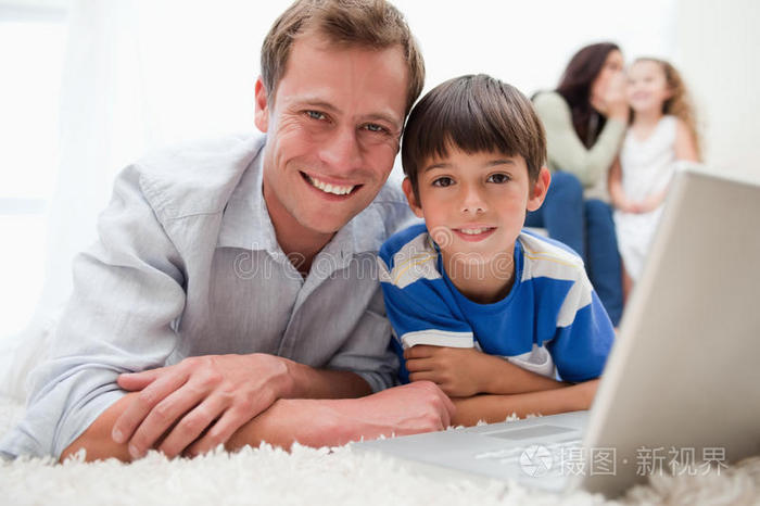 笑眯眯的儿子和爸爸在地毯上用笔记本电脑