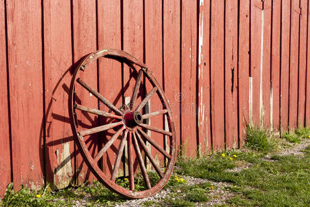 一个红色谷仓旁的老式马车轮子。