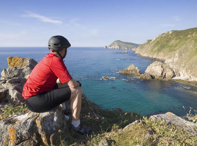 骑自行车的人坐着，盯着海岸风景