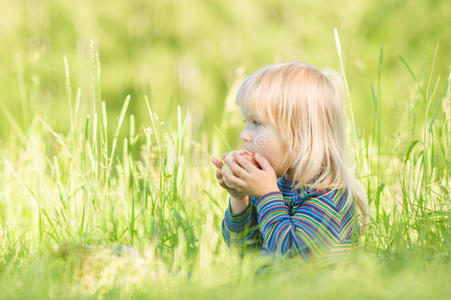 可爱的宝宝坐在草地上吃红苹果照片