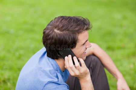 坐在公园里微笑的年轻人在打电话