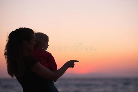 海滩上夕阳中带着孩子的母亲的剪影