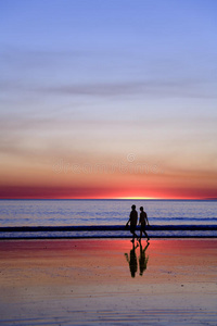 日落时分漫步在浪漫海滩上的年轻夫妇照片