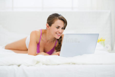快乐的年轻女人躺在床上用笔记本电脑