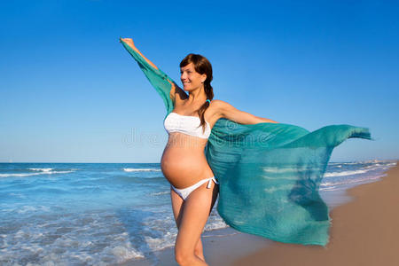 美丽的孕妇走在蓝色的沙滩上
