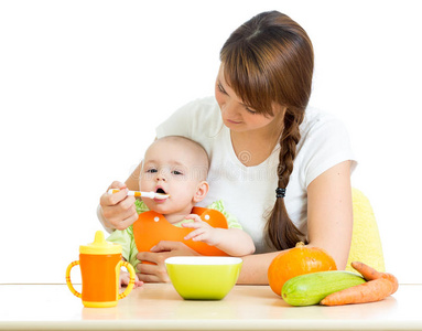 年轻的母亲在书桌上用勺子喂她的女婴