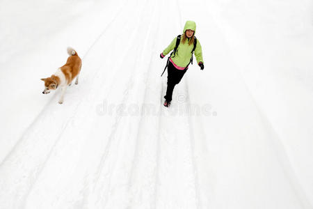 女人带着狗在冬天的路上和雪地上徒步旅行