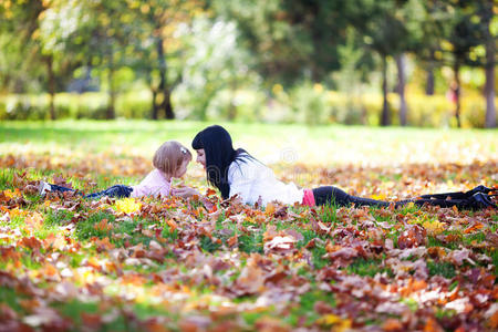 年轻的母亲和女儿躺在秋叶上
