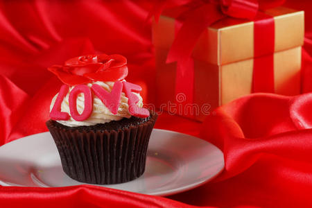 顶部有红玫瑰的纸杯蛋糕，红色缎子b的盒子里有礼物