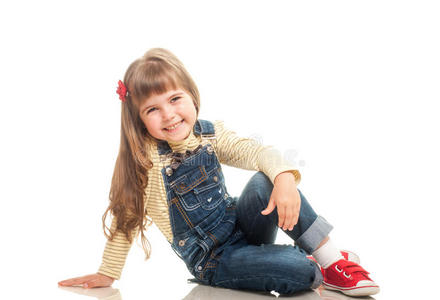 可爱的小女孩穿着牛仔裤坐在地板上