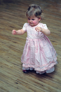 好奇的小女孩穿着粉红色的裙子走在木地板上