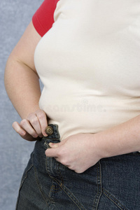 试图扣牛仔裤扣子的肥胖妇女照片