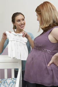 向怀孕的朋友展示婴儿衣服的妇女