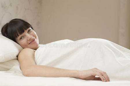 微笑的年轻孕妇躺在床上的画像照片