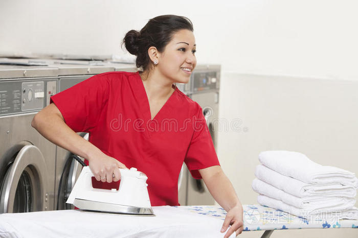 快乐的年轻女员工一边在自助洗衣店熨衣服