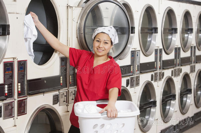 一位快乐的年轻女员工把衣服放进洗衣机的画像
