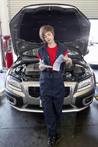 年轻的女机修工在车库里翻阅汽车引擎盖打开的报纸