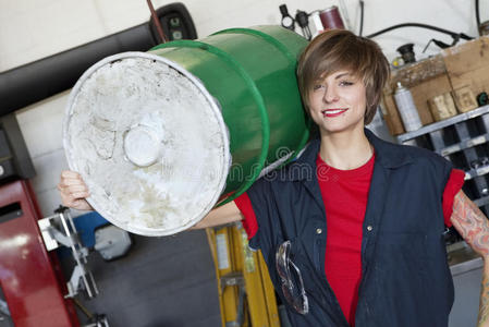 一位快乐的年轻女机修工肩上扛着油桶的画像