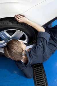 年轻机修工躺在地板上对汽车轮胎的高角度观察
