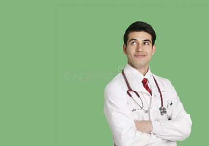 男医生身穿实验服，双臂交叉站在绿色背景下抬头看
