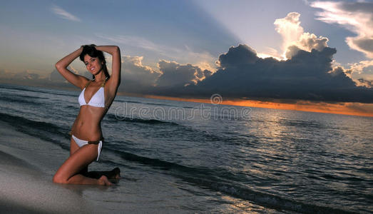 日出时坐在沙滩上的漂亮黑发模特