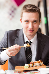 年轻英俊的商人用棍子吃寿司
