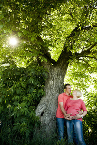 一对幸福的怀孕夫妇在坚果树下的画像。