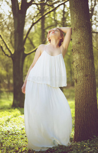 美丽的年轻新娘穿着白色婚纱对着树摆姿势