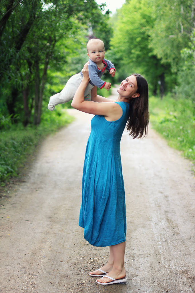 年轻的母亲在蓝色绿松石礼服举行她的小儿子在她的胳膊室外