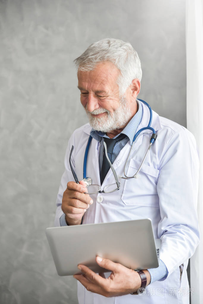 高级男性医生正在思考和检查他的病人病历在笔记本电脑在医疗室严重