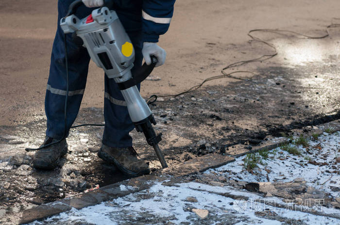 在城市的街道上工作的电钻的男人