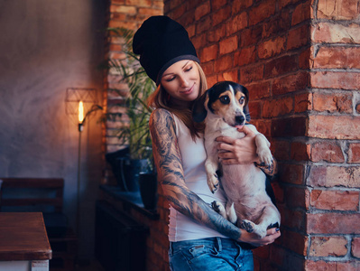 一个时尚的纹身金发女郎在 t恤衫和牛仔裤持有一只可爱的狗