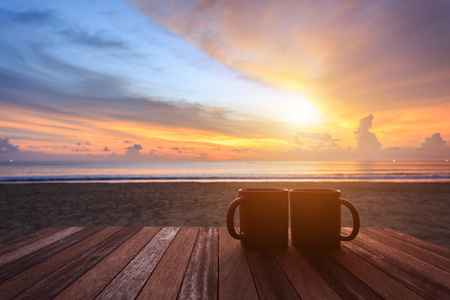 在日出或日落海滩的木桌上的咖啡杯